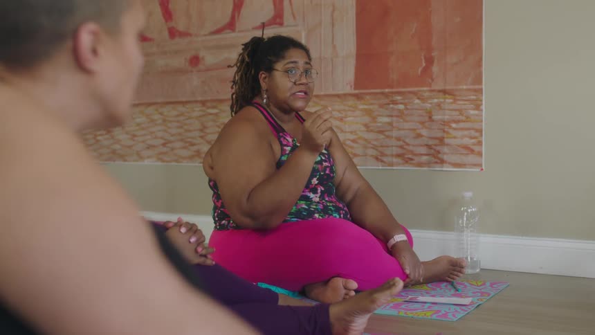 Group of barefoot women wearing sports clothes sitting over mats in the floor at home talking
