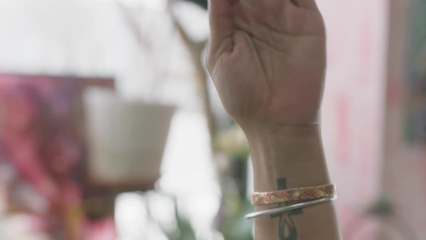A woman with a tattoo on her wrist calmly holds her hand up above her