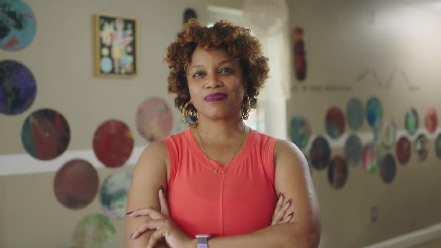 Black woman standing indoors near a window crossing her arms and smiling