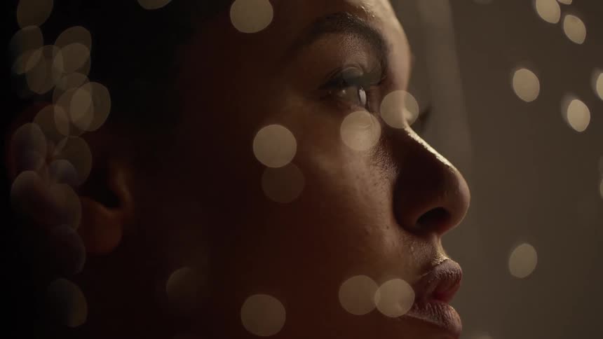A woman looks off into the distance while water droplets roll down a piece of glass in front of her