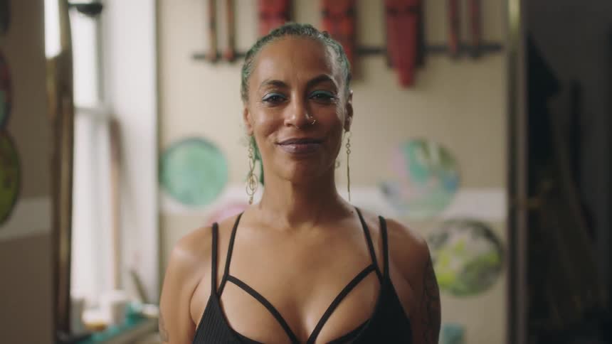 Black woman wearing makeup and earrings standing indoors smiling