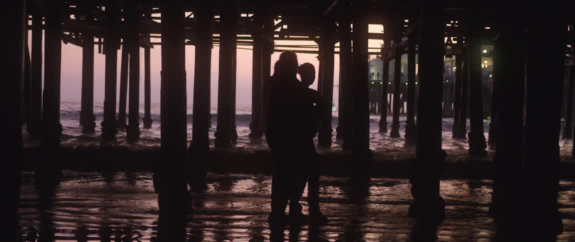Silhouette of a young couple hugging under a pier on the beach next to the ocean at sunset