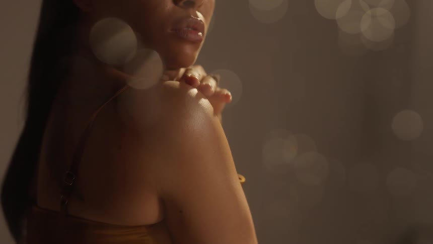 A woman posing caressing her own shoulder looking sexy as rain drops shimmer in the light