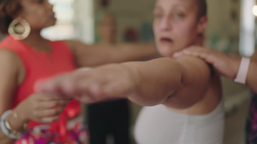 Woman holding a yoga pose surrounded by trainers correcting her pose at home