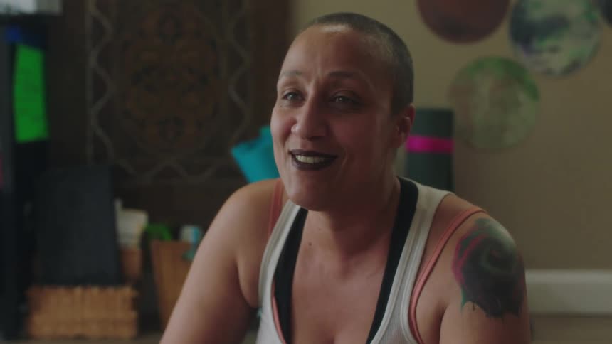 A woman sitting at home smiling and nodding her head wearing a tank showing off the shoulder tattoo