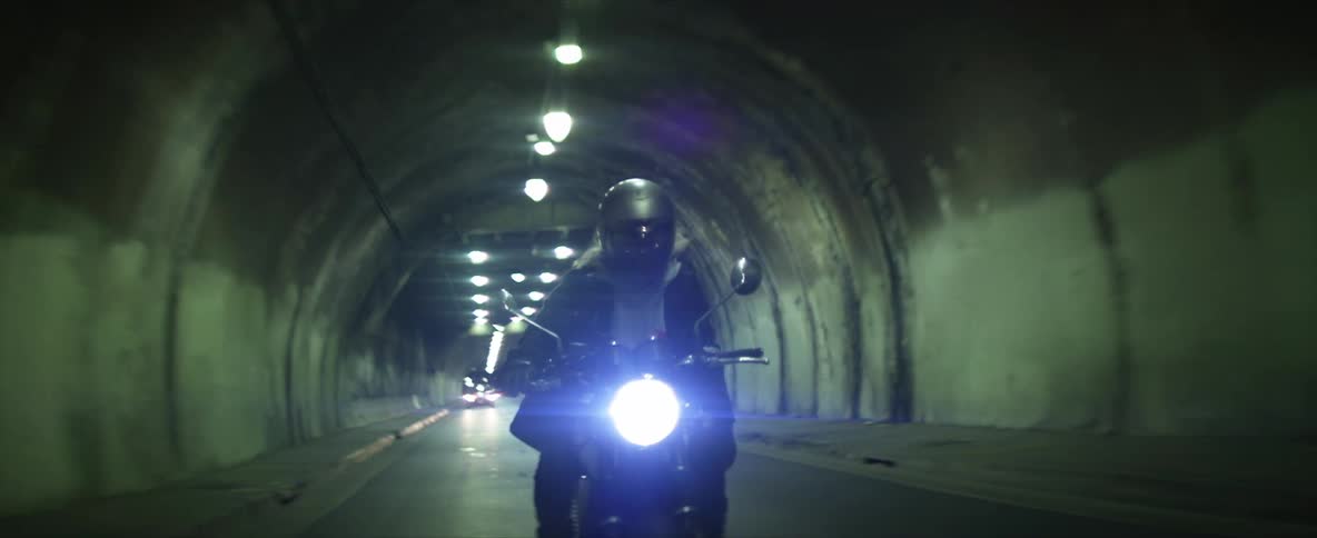 A person rides a motorcycle through a tunnel in a city at night