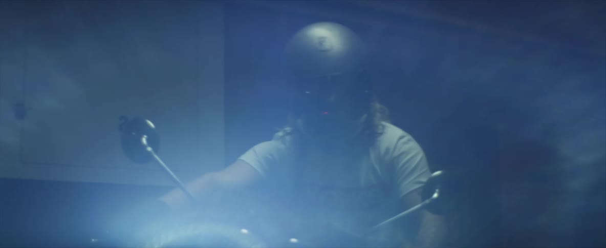 White man wearing a safety helmet mounting a motorcycle parked in a dark room