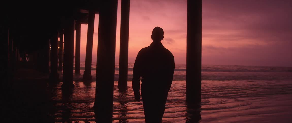 Woman walks under the pier silhouetted against a brilliantly colored red sky