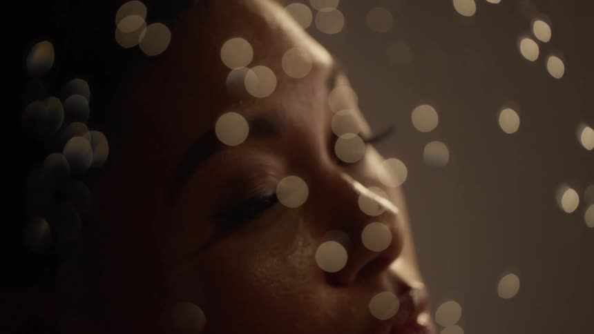 Young beautiful woman behind a glass with raindrops falling down looks at the camera