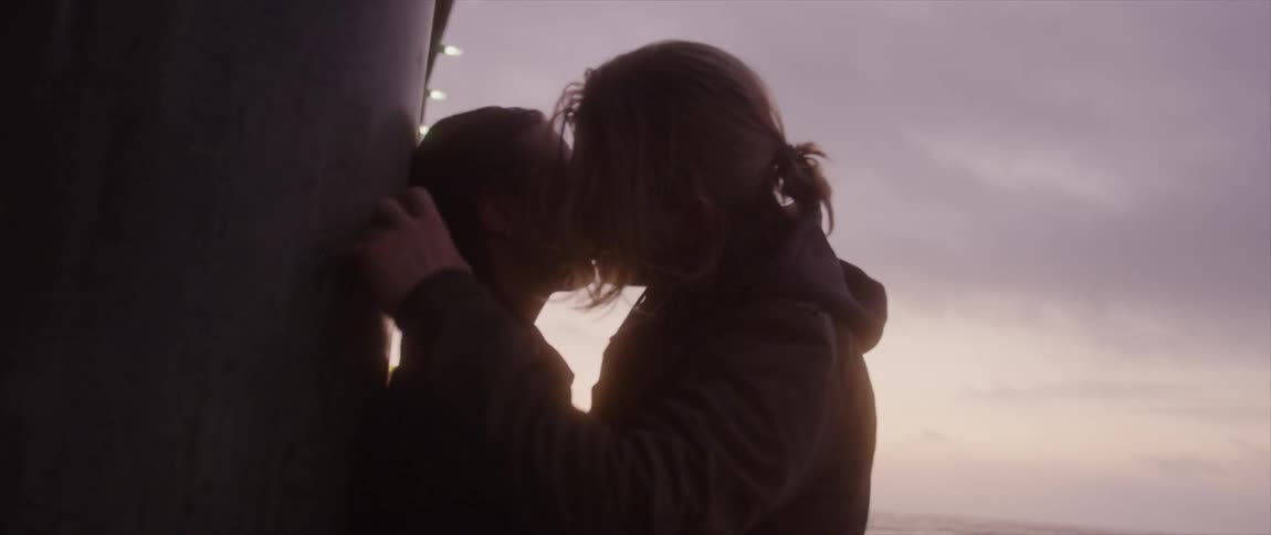 Silhouette of romantic couple kissing under the pier near the shoreline at sunset