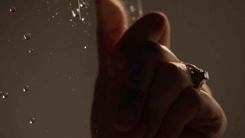 Hand with a diamond ring on a finger reclined on a wet window with water drops running down