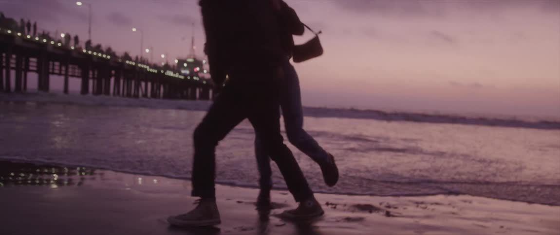 Couple holding and cuddling each other is silhouetted against the purple sky on the beach next to pier
