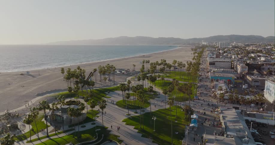 People walk on the walkways next to the beach as mountains sit in the distance