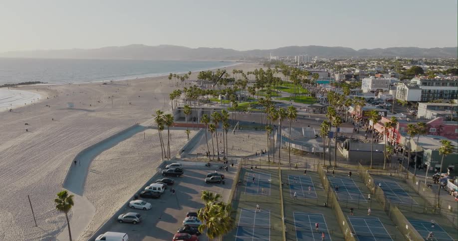 Aerial view of tennis courts next to car park and vast beach with coastal city