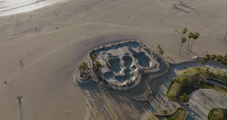 People move along park beach and skate park as ocean water reflects the sunlight