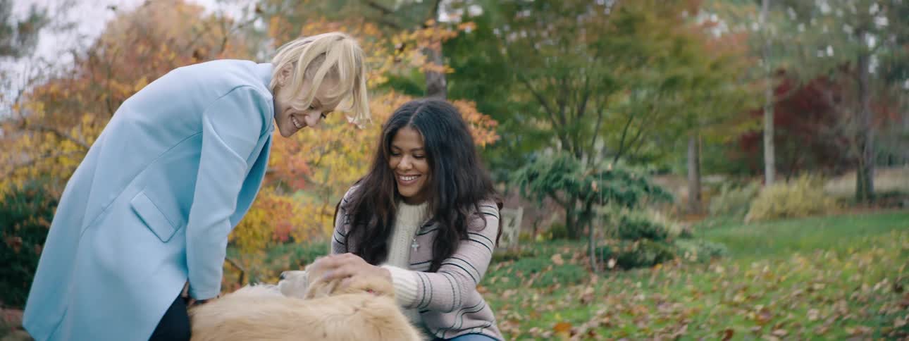 Two friends play with a golden retriever in a garden with fall colors