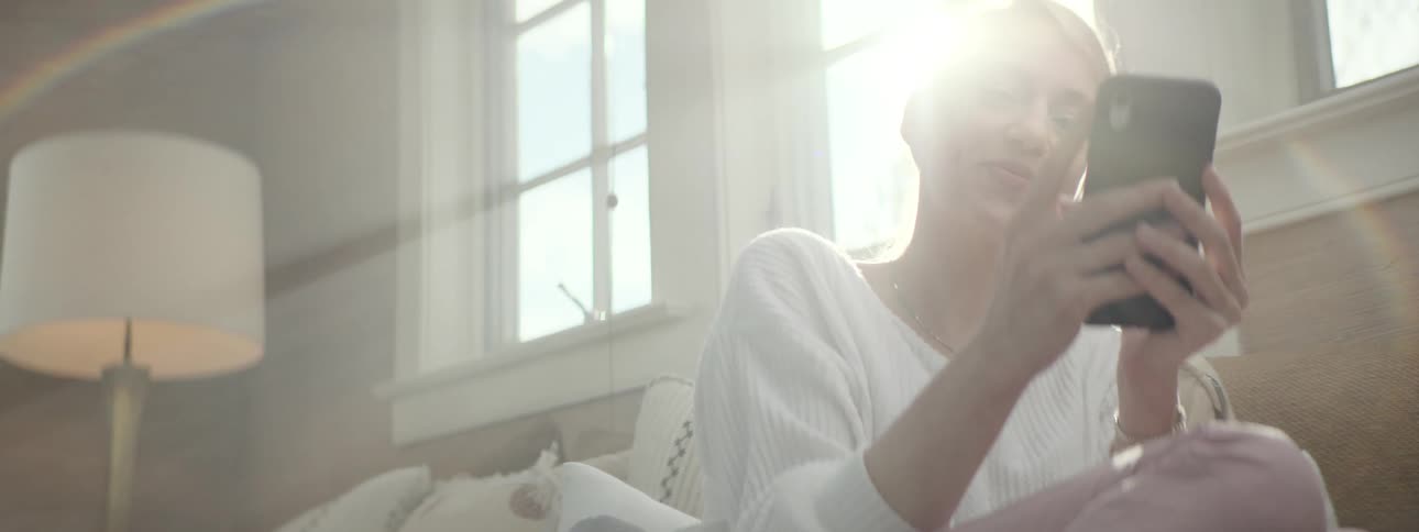 Young woman engages in laughter with someone on her cell phone in a light filled living room