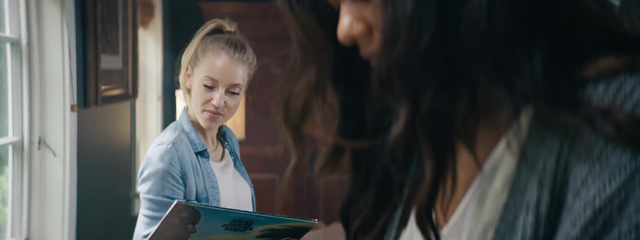 Two female friends hang out and look through records together in a moody library