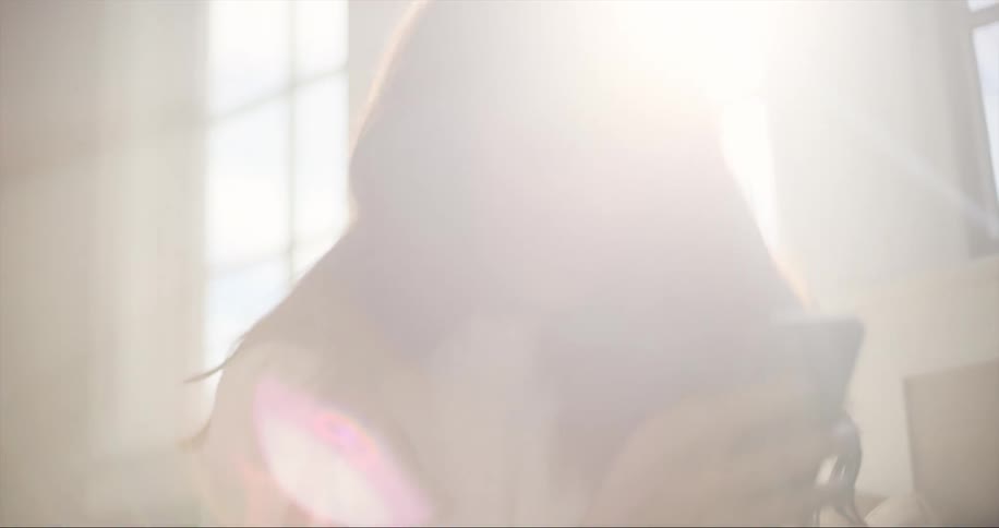 Woman with dark wavy hair and white sweater uses smartphone sitting on couch while the sun shines through windows