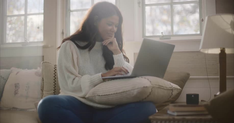 A woman is sitting in a living room and typing on a laptop