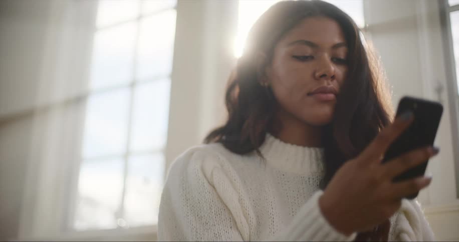 A woman smiles as she holds her phone and looks at the screen