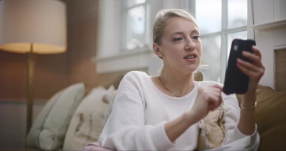 A woman scrolls through her smartphone while sitting on the couch
