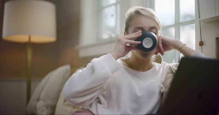 Young woman working from home with her laptop and drinking a cup of coffee