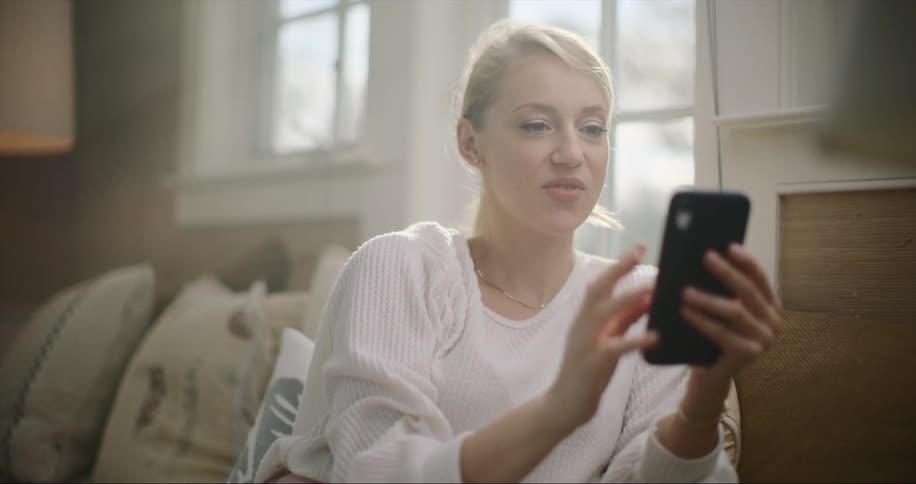 Blonde woman sitting on the couch next to the window using her phone