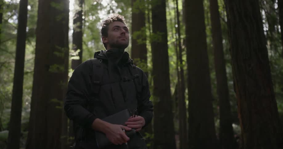 Man stands in a forest holding a notebook and pen