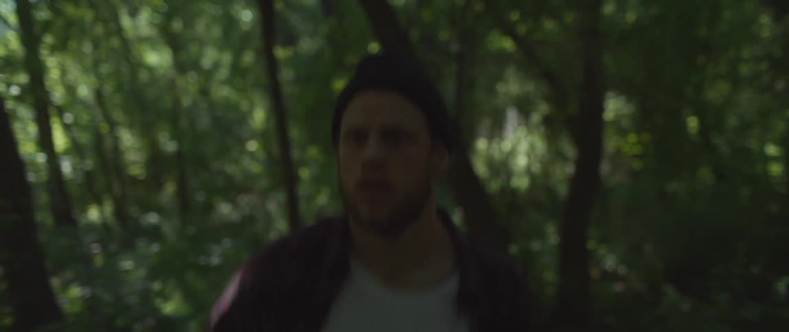 Man wearing knit hat runs through woods