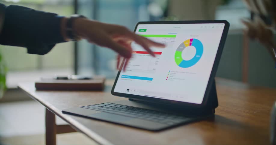 Hand of a man pointing to the screen of a laptop placed at a table showing a pie chart  and some stats