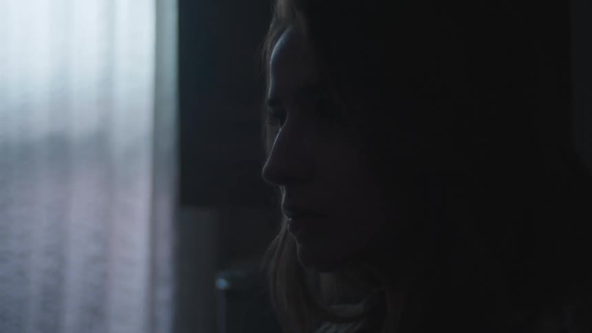 Woman with brown wavy hair is silhouetted against the window light in room