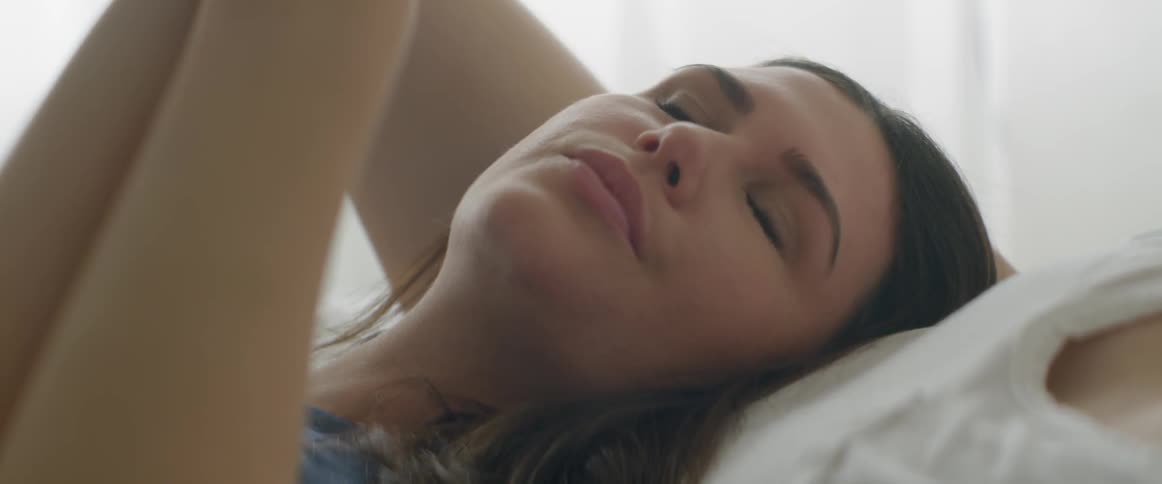 Woman lays in bed next to someone touching her hair