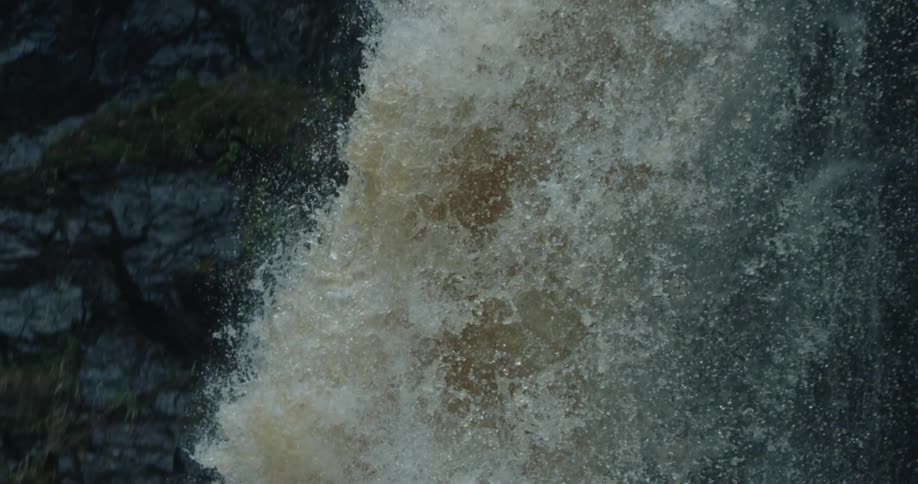 Slow motion footage of a powerful waterfall running down a rock wall over a river