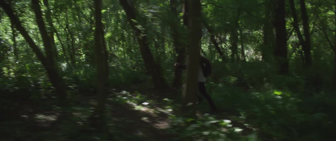 Man with wooly hat dark and white shirt and black pants runs away in the green forest