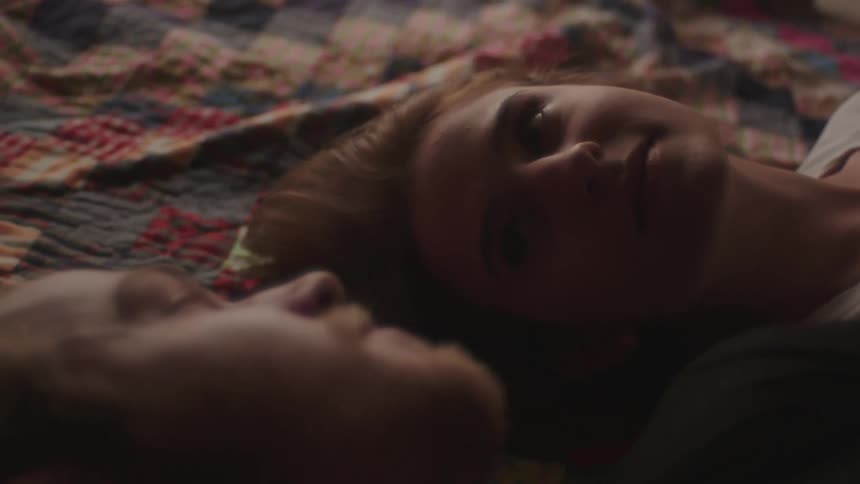 A man and woman lying side by side on a blanket gaze at one another