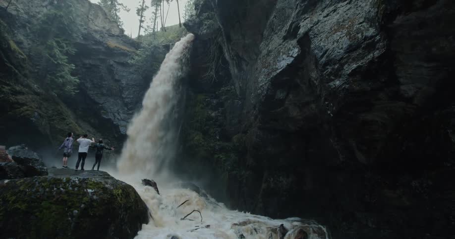 Three friends standing on a rock in front of a powerful waterfall in a canyon
