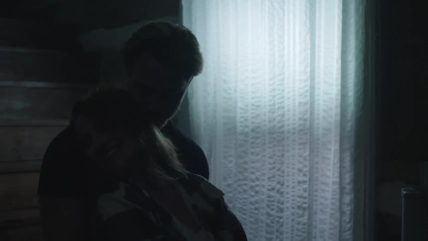 Man back hugs woman as they sway side to side in dimly lit room