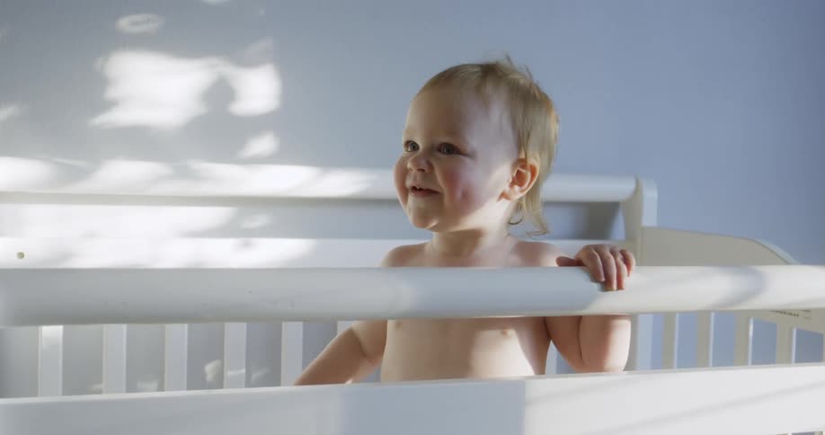 A baby smiles while standing in a crib