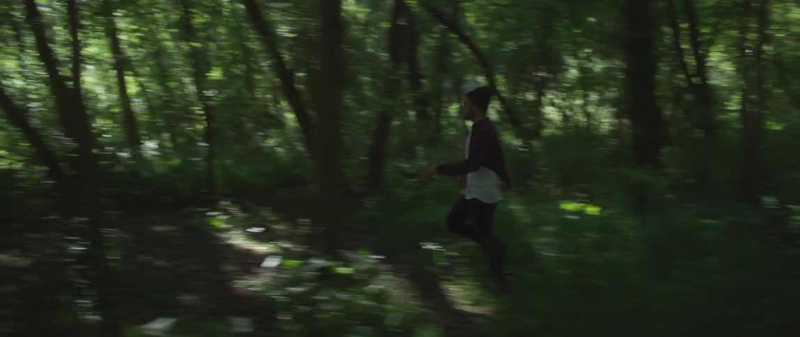 Man with wooly hat dark and white shirt and black pants runs away in the woods