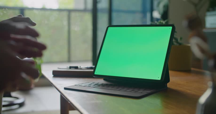 Green screen on a computer monitor with two pairs of hands that are clenching fingers in front of it