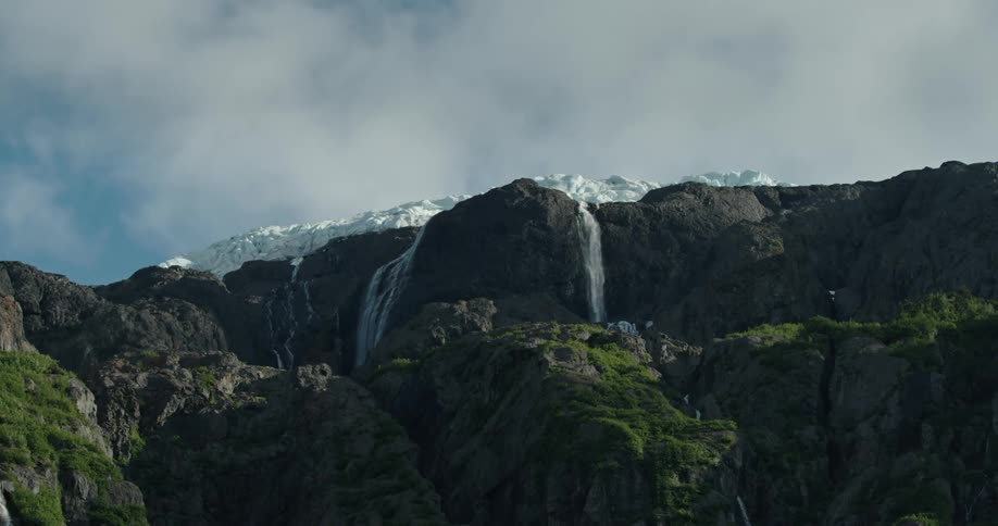 Distant waterfall cascades down high mountainside from a glacier