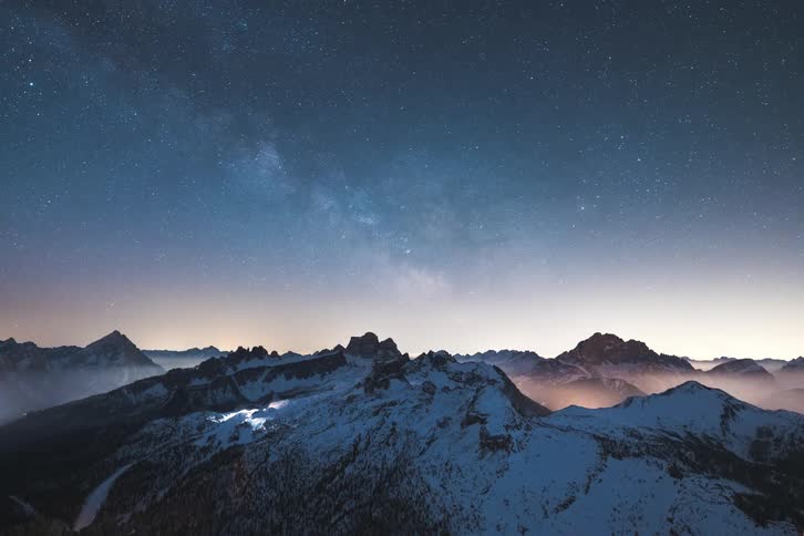 Shadow flows across the snow covered mountains as night falls revealing glowing fog