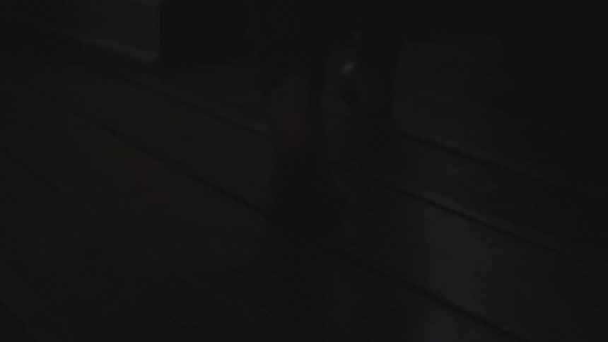 Barefoot person walking over a wooden floor inside a dimly lit room