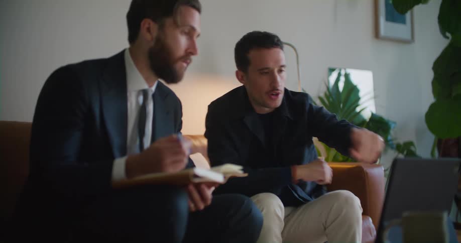 Two men having a business meeting in the living room looking at a tablet over the coffee table