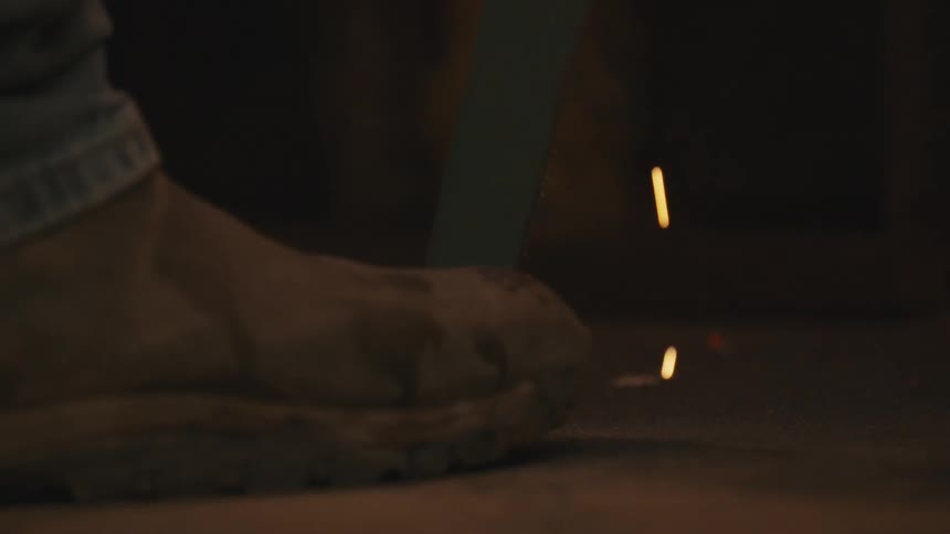 Sparks fall onto the floor in front of a boot