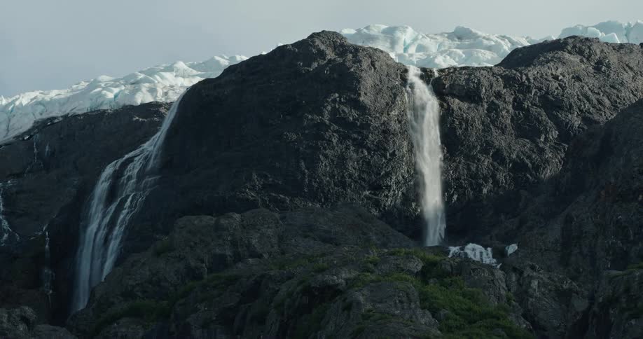 Waterfalls flow down the sides of a mountain and from a snow covered rocky peak