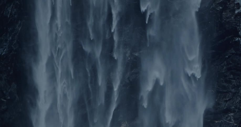 A massive waterfall cascades down a rock wall in slow motion