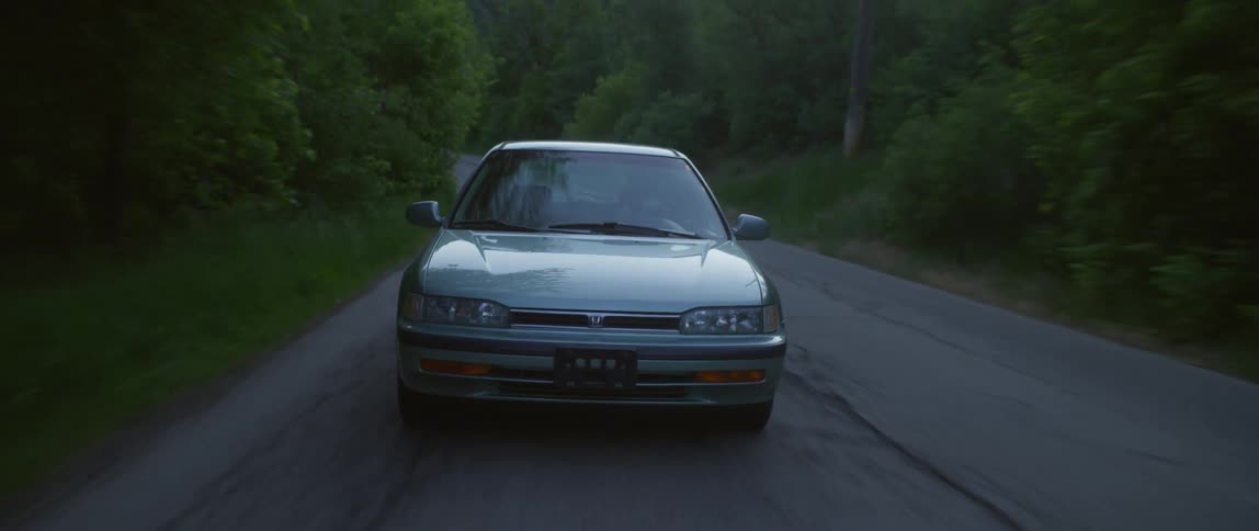 A car travels along a road through a woodland during the day