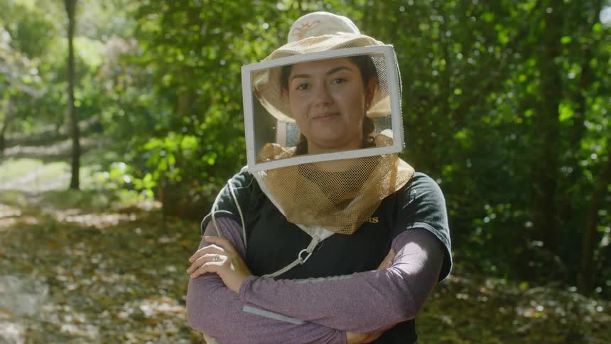 A beekeeper poses for a photo and crosses her arms and smiles
